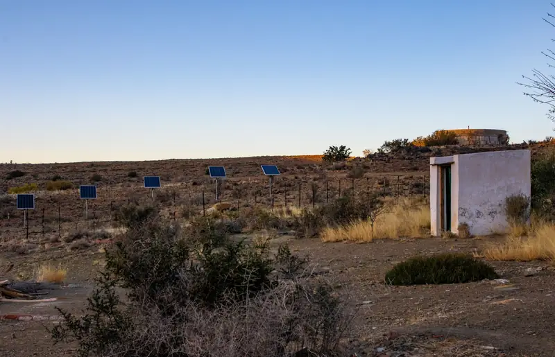 Pole-mounted solar panels beside a pump house in arid scrubland